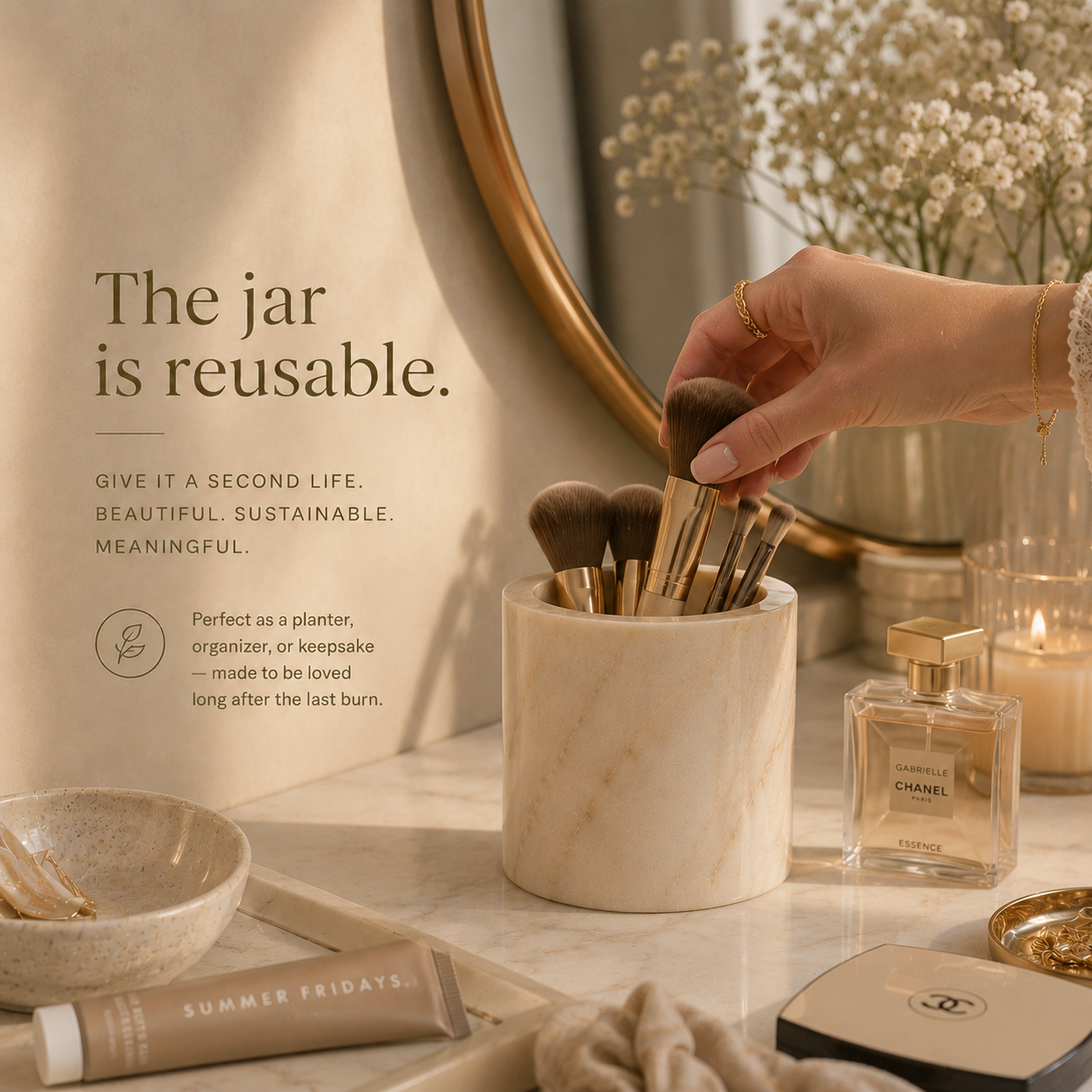 Hand holding makeup brushes in a reusable jar on a vanity with decorative items. Reusable natural marble candle jar by IVARO designed as a lasting luxury home decor object